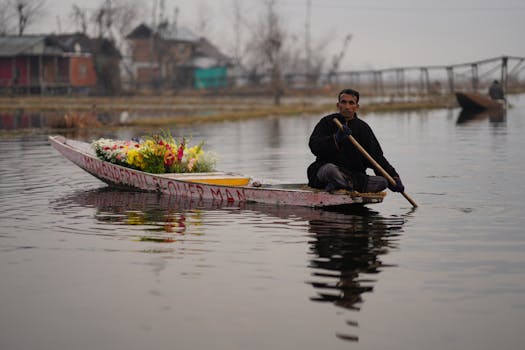 A man paddles a boat filled with vibrant flowers on a serene lake, showcasing a peaceful lifestyle.