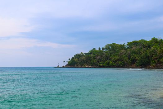 Serene tropical coastline with lighthouse and lush greenery in Andaman, India.